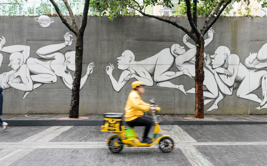 Yellow-clad scooter rider drives past a concrete wall sprayed with graffiti art in Shenzhen