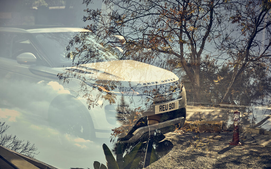 Range Rover Evoque 2019 Testfahrt: Roadtrip durch Athen Range Rover Evoque auf Straße mit Olivenbäumen spiegelt sich in Scheibe eines anderen Pkw