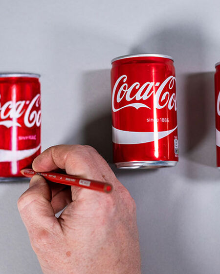 Howard Lees Hand zeichnet eine originalgetreue Cola-Dose, neben der zwei echte Cola-Dosen liegen