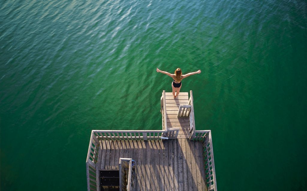 Interview Iris Schmidbauer im "Strandbad Utting" Iris Schmidbauer steht auf Sprungbrett mit ausgebreiteten Armen über dem Ammersee in Utting