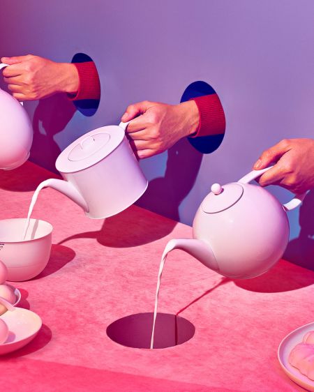 Hände halten drei Kaffeekannen und gießen daraus Flüssigkeit in Porzellangefäße