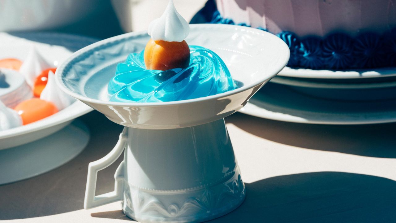 Close-up of a plate with blue jelly and a fruit, standing on an upside-down cup.