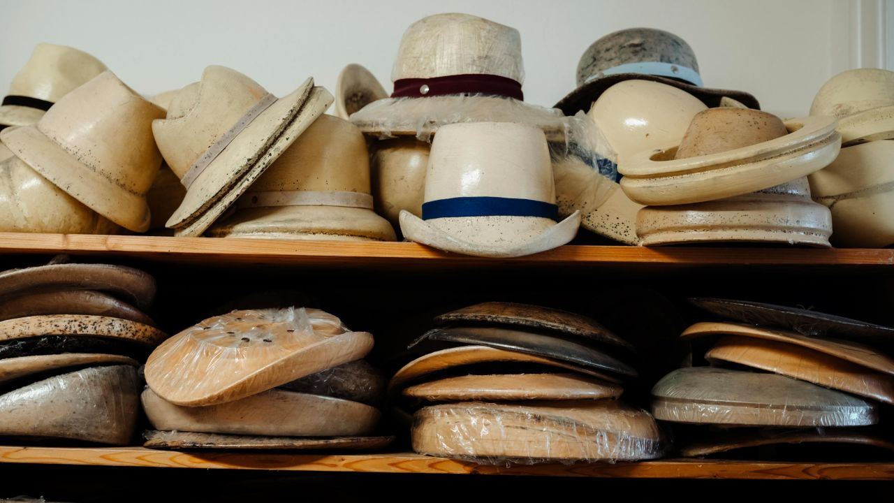 Eine Ablage mit mehreren Reihen von fertigen und unfertigen Hüten sowie Hutformen in verschiedenen Größen.