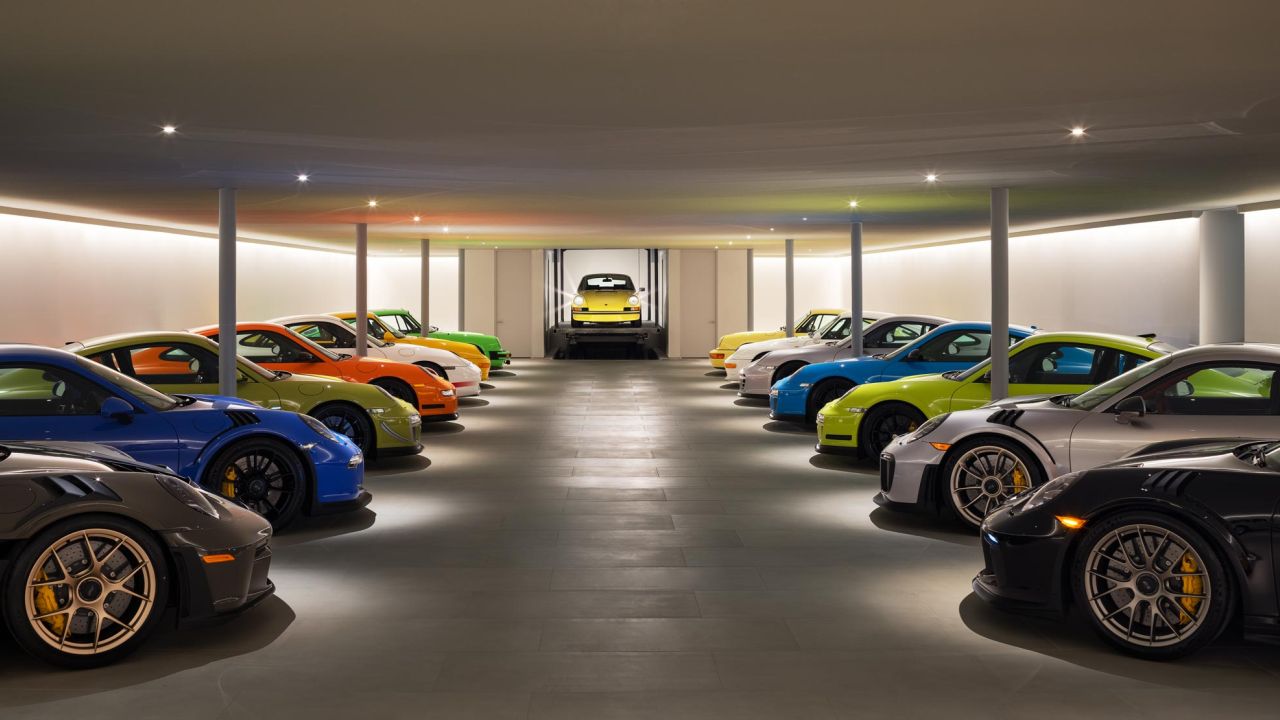 Eine große Sammlung farbenfroher Porsche-Sportwagen steht in einer Reihe in einer modernen Garage