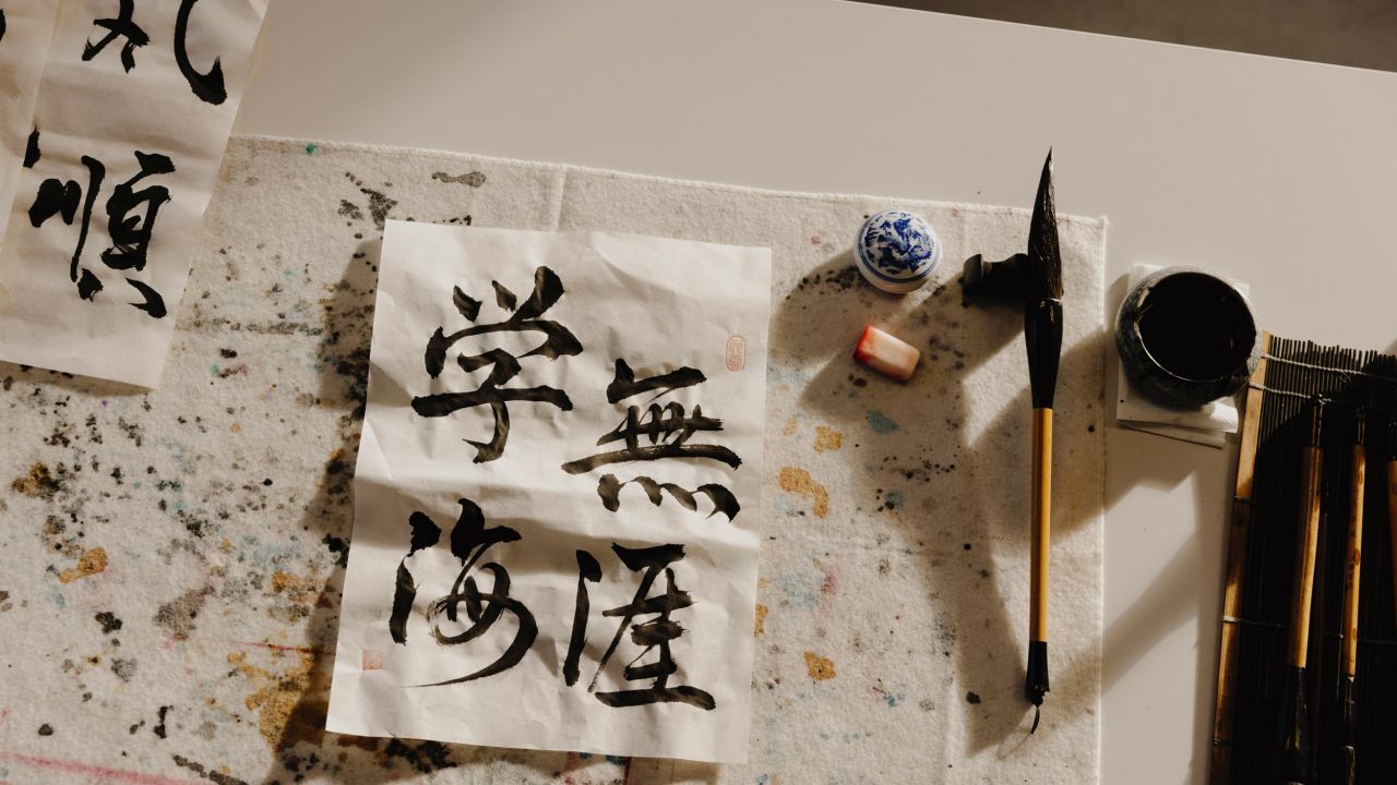 Nahaufnahme eines Tisches mit Pinsel für Kalligrafie, Tinte und einem gefalteten Papier mit chinesischen Schriftzeichen