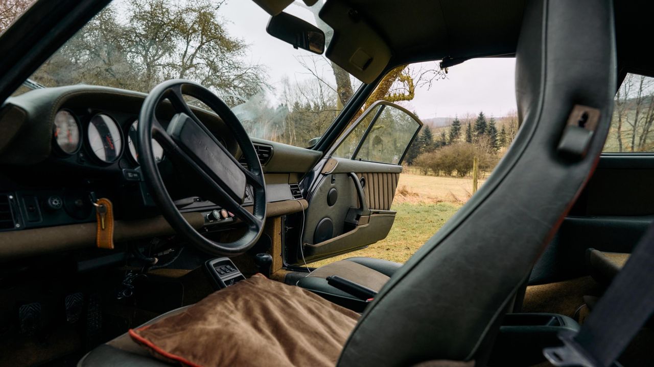 Innenansicht eines grünen Porsche 911 mit schwarzem Ledersitz, beigem Sitzkissen und geöffneter Tür Innenansicht eines grünen Porsche 911 mit schwarzem Ledersitz, beigem Sitzkissen und geöffneter Tür